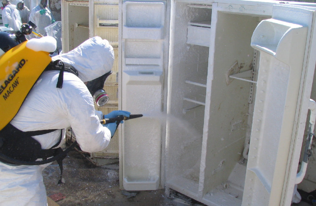 Man in hazmat suit with sprayer unit backpack spraying into a refrigerator